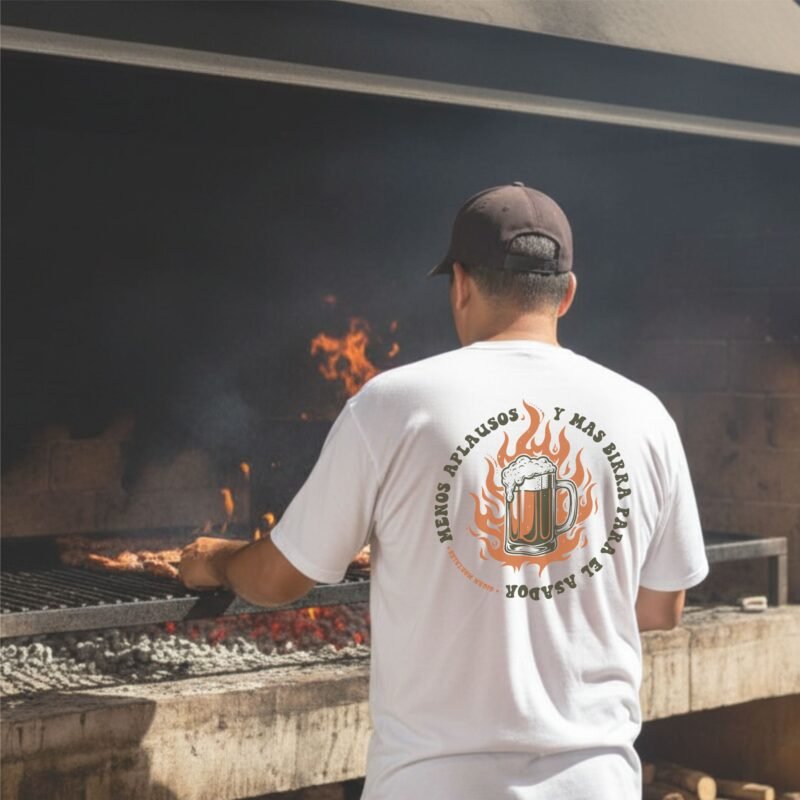 hombre haciendo asado con una remera blanca argentina que dice menos aplausos y mas birra cerveza para el asador
